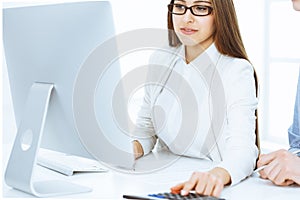 Young business woman and man sitting and working with computer and calculator in office. Bookkeeper checking balance or