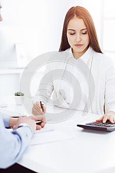 Young business woman and man sitting and working with computer and calculator in sunny office. Bookkeeper checking