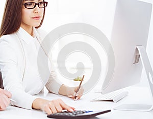 Young business woman and man sitting and working with computer and calculator in sunny office. Tax and audit concepts