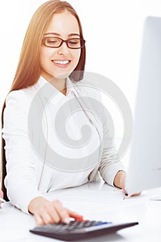 Young business woman and man sitting and working with computer and calculator in sunny office. Tax and audit concepts