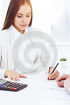 Young business woman and man sitting and working with computer and calculator in sunny office. Tax and audit concepts