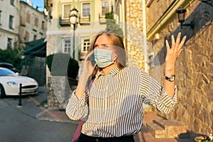 Young business woman in medical protective mask talking on smartphone outdoors