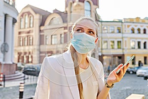 Young business woman in medical protective mask talking on smartphone