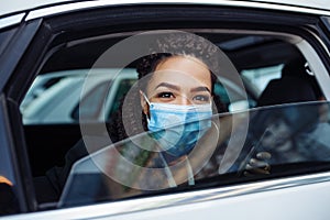 Young business woman passenger wearing a medical mask looks out of a taxi car window. Business trips during pandemic, new normal