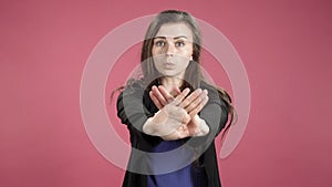 Young business woman showing stop sign against pink background. Denying, rejecting, disagree.