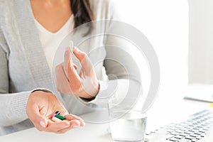 Young business woman sick in the office, hand holding pills