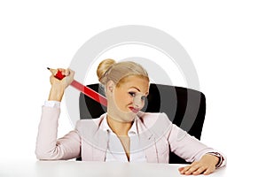 Young business woman sitting behind the desk and holding big pen