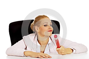 Young business woman sitting behind the desk and holding big pen