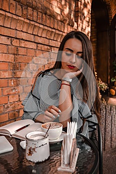 Young business woman sitting in cafe drinking coffee. Beautiful girl is working against an orange brick wall. View of freelancer