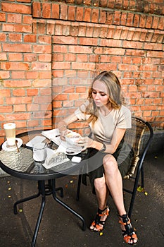 Young business woman sitting in cafe drinking coffee. Beautiful girl is working against an orange brick wall. View of freelancer