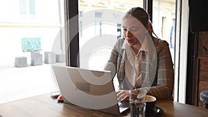 Young business woman sitting in the coffee shop during the lunch break drinking coffee and work on the laptop computer. Freelancer