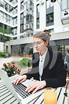 Young business woman sitting at coffee shop on veranda and working on laptop