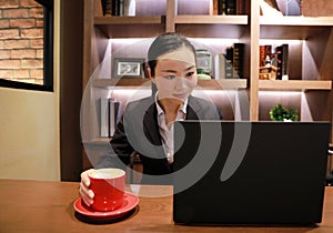 Young business woman sitting in coffee shop at wooden table, drinking coffee .On table is laptop