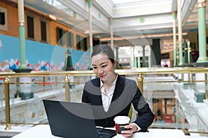 Young business woman sitting in coffee shop at wooden table, drinking coffee .On table is laptop