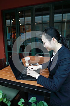 Young business woman sitting in coffee shop at wooden table, drinking coffee . On table is laptop