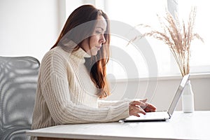 Young business woman sitting at desk working online on laptop