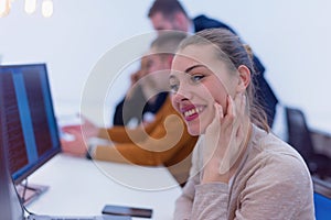 Young business woman sitting at her desk and smiling.  Happy successful business leader working while her team in background