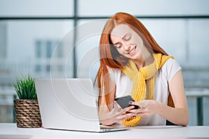 Business woman sitting in office, looking at graphics and uses smartphone