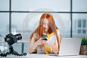 Business woman sitting in office, looking at graphics and uses smartphone