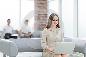 Young business woman sitting at sofa and working with laptop