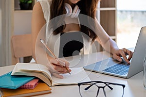 Young business woman sitting at table and taking notes in notebook.On table is laptop, smartphone and cup of coffee.On