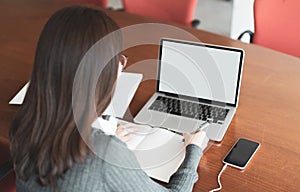 Young business woman sitting at table and taking notes in notebook, On table is laptop, Smartphone and cup of coffee, Student lear