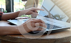 Young business woman sitting on wooden table at the coffee cafe and using modern laptop working and her finger is pointing at the