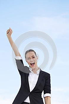 Young business woman standing against blue sky, with one arm in the air