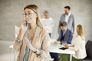 Young business woman standing in the office and suing mobile phone in front of her team