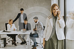 Young business woman standing in the office and using mobile phone in front of her team