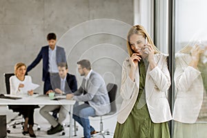 Young business woman standing in the office and using mobile phone in front of her team