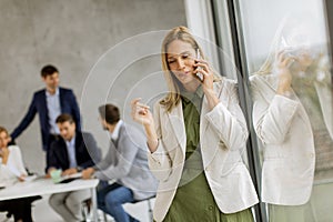Young business woman standing in the office and using mobile phone in front of her team