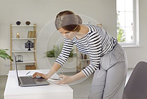 Young business woman standing by office work desk and using laptop and mobile phone