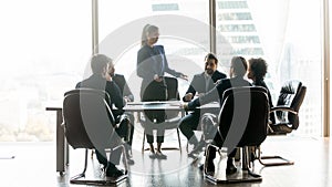 Young business woman standing at table, talking to diverse colleagues.