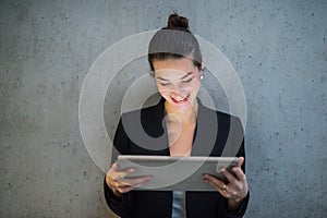 Young business woman with tablet standing against concrete wall in office.