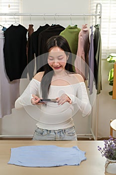 Young business woman takes a photo of a cloth with her smartphone device to put it up for sale on a second-hand clothing