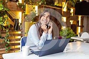 Young business woman using her laptop at a cafe. Beautiful woman sitting at a table with a cup of coffee and mobile phone surfing