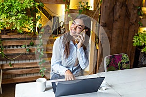 Young business woman using her laptop at a cafe. Beautiful woman sitting at a table with a cup of coffee and mobile phone surfing