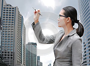 Young Business woman using pen writing on air against building background, Business Concept