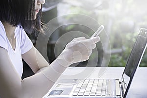 Young business woman using smart phone with laptop computer while sitting on white table