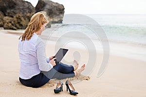 Business woman using tablet computer while sitting on the beach