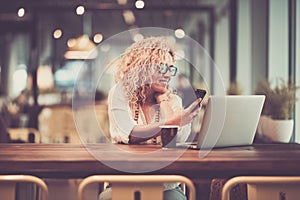 Young business woman in video conference call with phone and laptop computer sit down at bar cafe in the airport waiting to flight