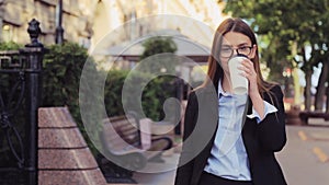 Young business woman is walking on the street and drinks coffee and using smartphone at lunch break.