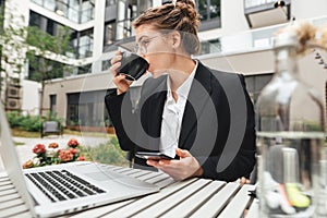 Young business woman wearing glasses at cafe using laptop and drinking coffee