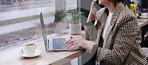 Young business woman wearing suit talking on the phone and working on a laptop in a cafe. Work online. Distance learning. Copy