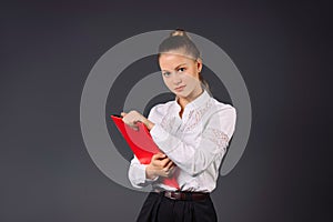 A young business woman in a white shirt and a red folder is looking at the camera against a gray background with empty