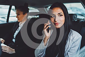 Young business woman witting in the back of a car with a colleague, talking on the phone and looking out the window