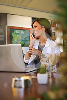 Young business woman working at cafe. Drinking coffee and talking on smart phone.