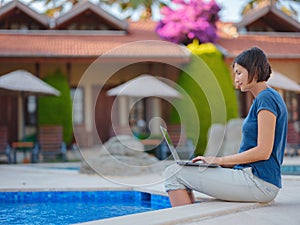Young business woman working at computer by hotel pool