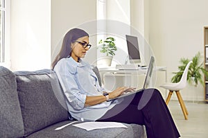 Young business woman working with laptop computer at home sitting on sofa.